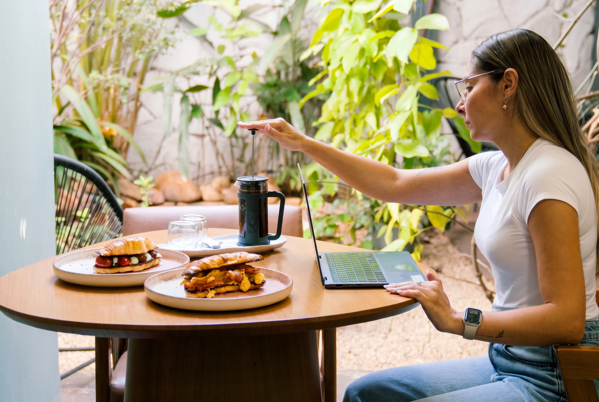 Cliente no jardim do Lumne Bistrô preparando café à mesa com pratos da casa